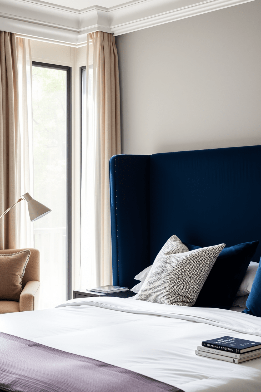 A chic bedroom design featuring a stylish upholstered headboard in a deep navy blue. The bed is adorned with crisp white linens and a mix of textured throw pillows for added comfort. Natural light floods the room through sheer curtains, illuminating a cozy reading nook with a plush armchair. A minimalist nightstand holds a modern lamp and a stack of books, enhancing the inviting atmosphere.