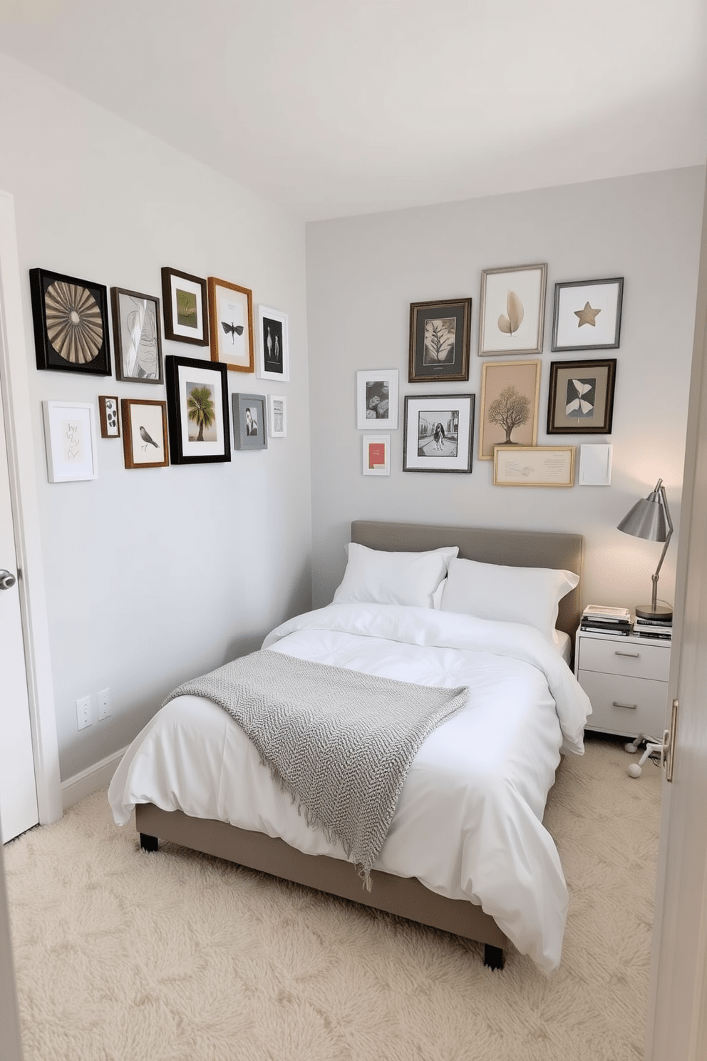 A cozy 10x10 bedroom featuring a soft color palette with light gray walls and a plush white carpet. On one wall, a collection of decorative wall art pieces adds a personal touch, showcasing various styles and frames that reflect the owner's personality. The bed is positioned against the opposite wall, dressed in crisp white linens and a textured throw blanket. Beside the bed, a sleek nightstand holds a stylish lamp and a small stack of books, creating an inviting and functional space.