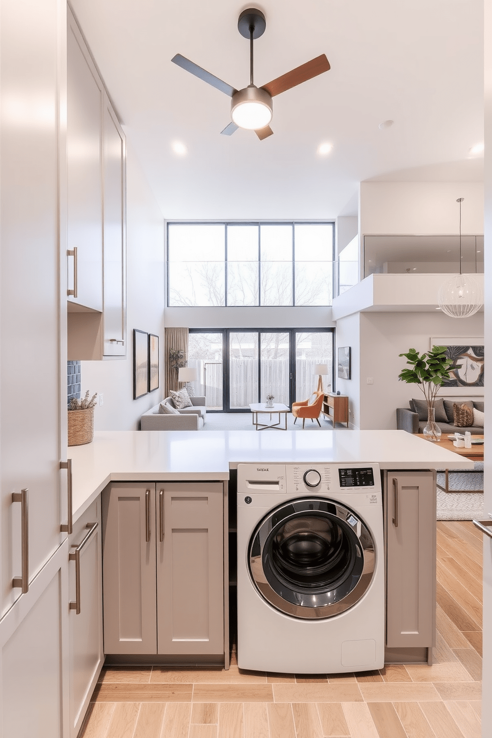 A functional laundry room with ample storage features sleek cabinetry in a soft gray finish. The space includes a large countertop for folding clothes and a stylish backsplash that adds a pop of color. In a two-story apartment design, the open-concept living area seamlessly connects to the kitchen and dining space. Large windows fill the room with natural light, highlighting the modern furnishings and warm wood accents.