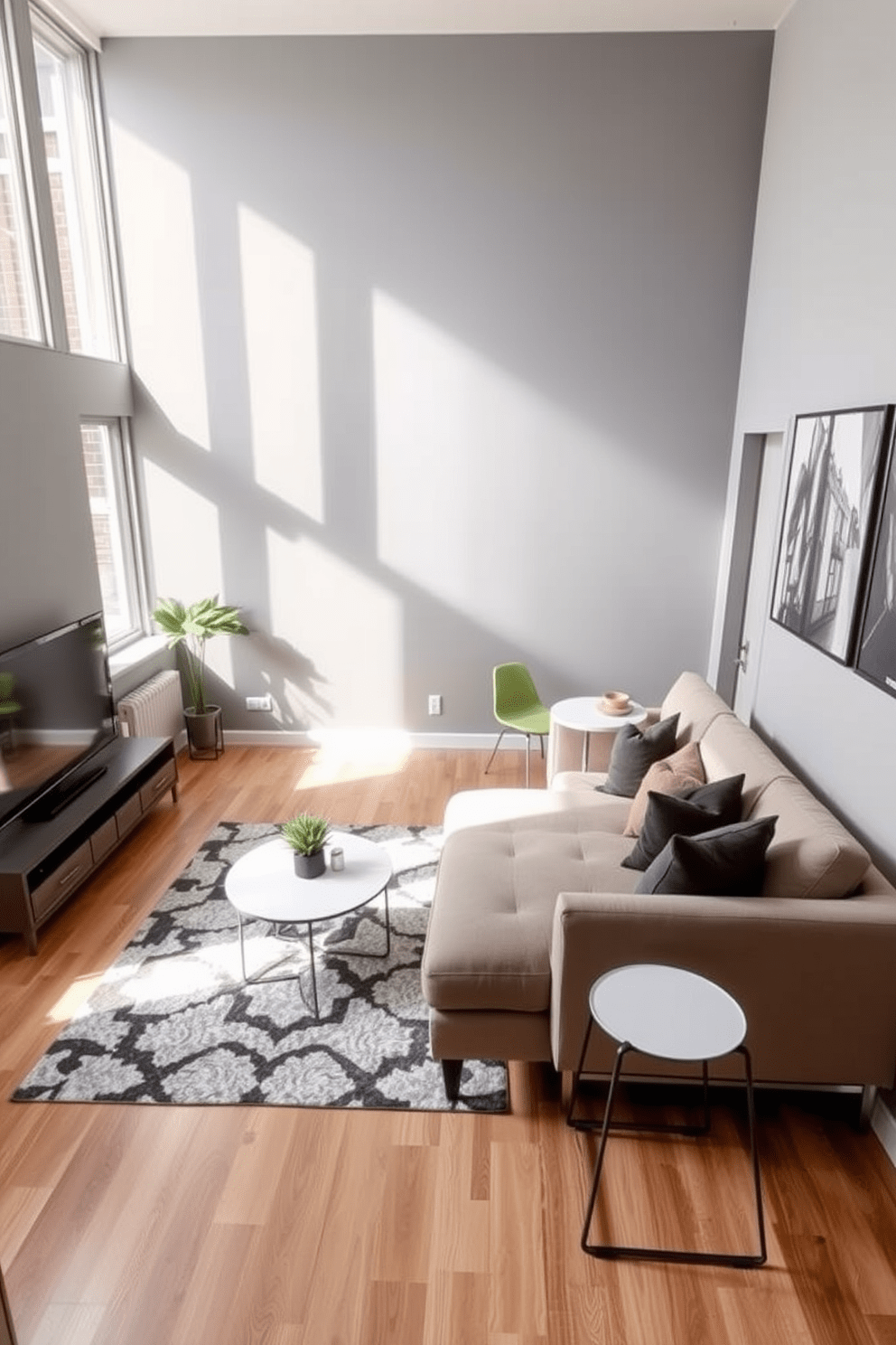 A modern living room in a 500 square foot apartment featuring a wall-mounted TV to maximize space efficiency. The room includes a sleek sectional sofa in a neutral color, a minimalist coffee table, and a stylish area rug that adds warmth to the space. The walls are painted in a soft gray hue, complementing the natural light streaming through large windows. A small dining nook with a round table and two chairs is positioned near the kitchen, creating an inviting atmosphere for meals and gatherings.