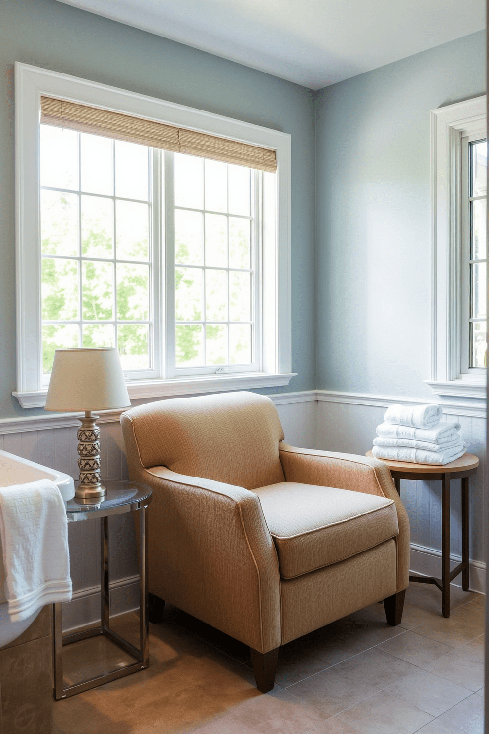 A comfortable seating area in a bathroom designed for accessibility features a plush armchair upholstered in a water-resistant fabric. The chair is positioned near a large window that allows natural light to fill the space, creating a warm and inviting atmosphere. Next to the armchair, a small side table holds a decorative lamp and a stack of soft towels. The walls are painted in a soothing light blue, and the floor is covered with non-slip tiles for safety and comfort.