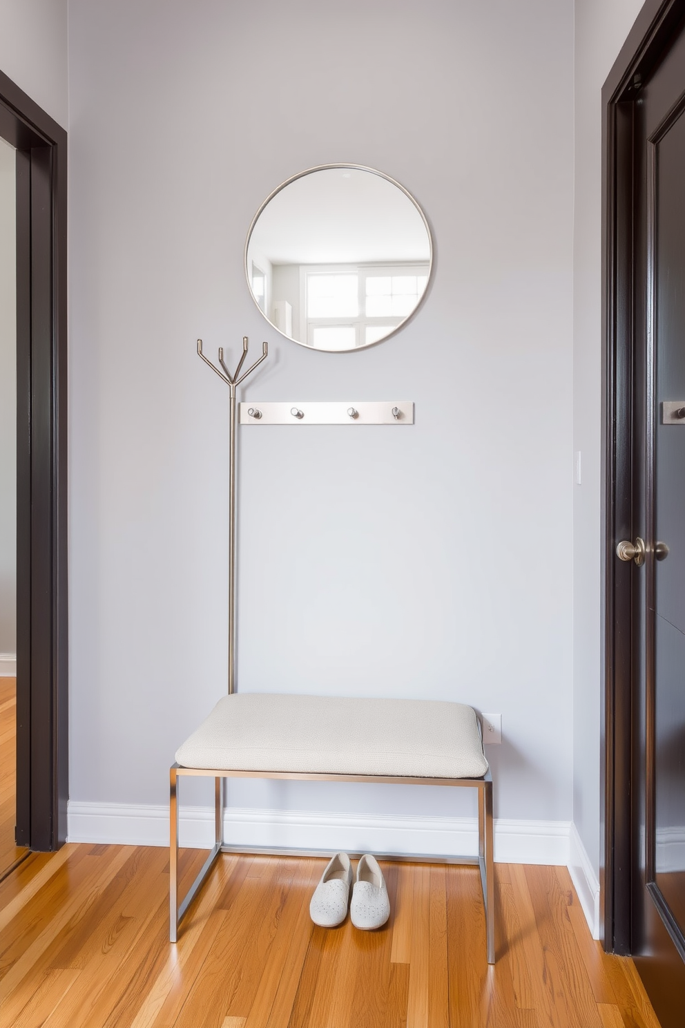 A stylish apartment entryway features a small coat rack made of sleek metal, positioned against a soft gray wall. Beneath the coat rack, a minimalist bench with a plush cushion invites guests to sit while removing their shoes. The floor is adorned with a warm wood finish, adding a touch of elegance to the space. A round mirror hangs above the bench, reflecting natural light and creating an inviting atmosphere.