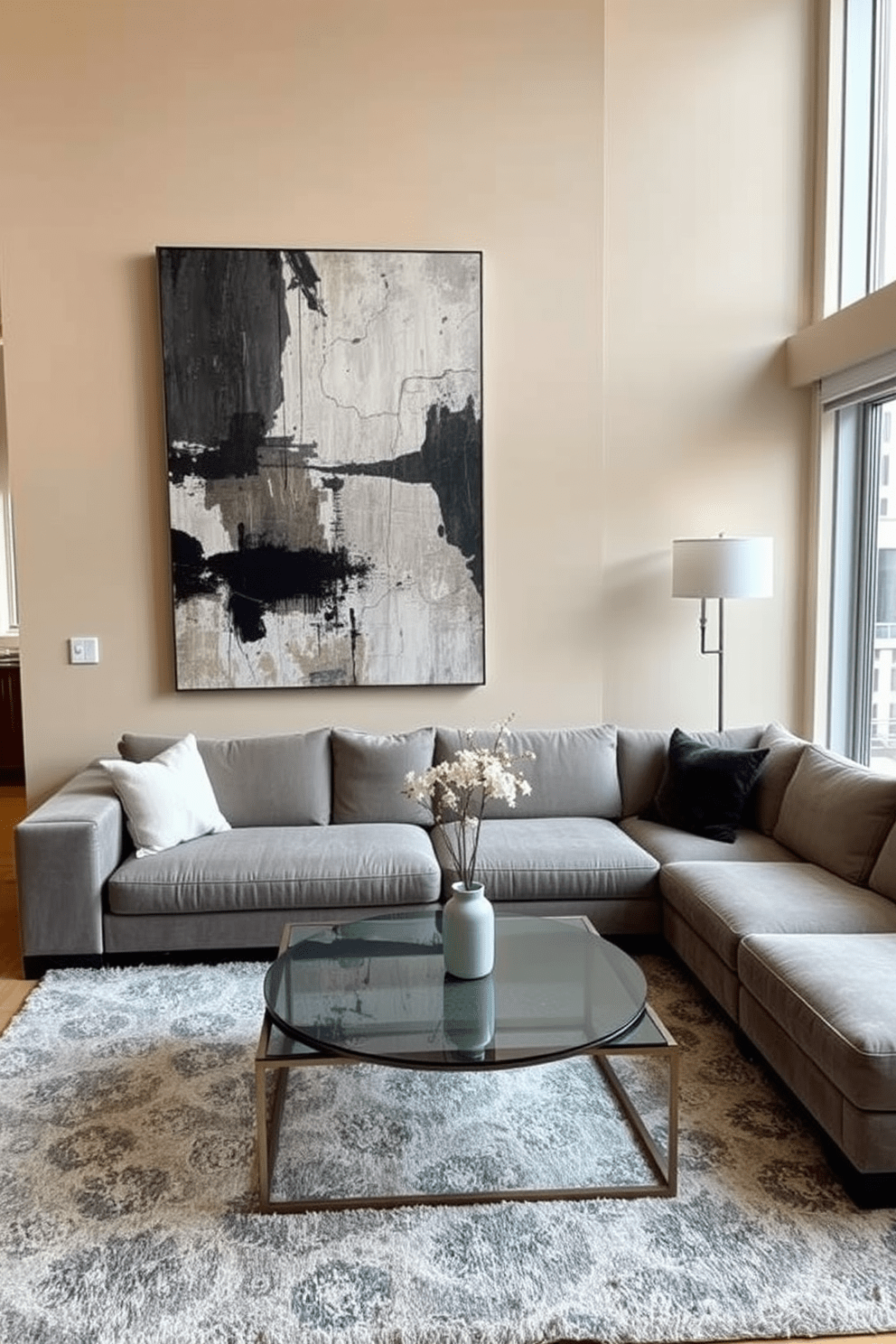 A stylish apartment living room featuring a statement coffee table at the center. The coffee table is made of glass and metal, surrounded by a plush sectional sofa upholstered in a soft gray fabric. The walls are painted in a warm beige tone, complemented by a large abstract painting above the sofa. A cozy area rug anchors the space, while floor-to-ceiling windows allow natural light to flood the room.