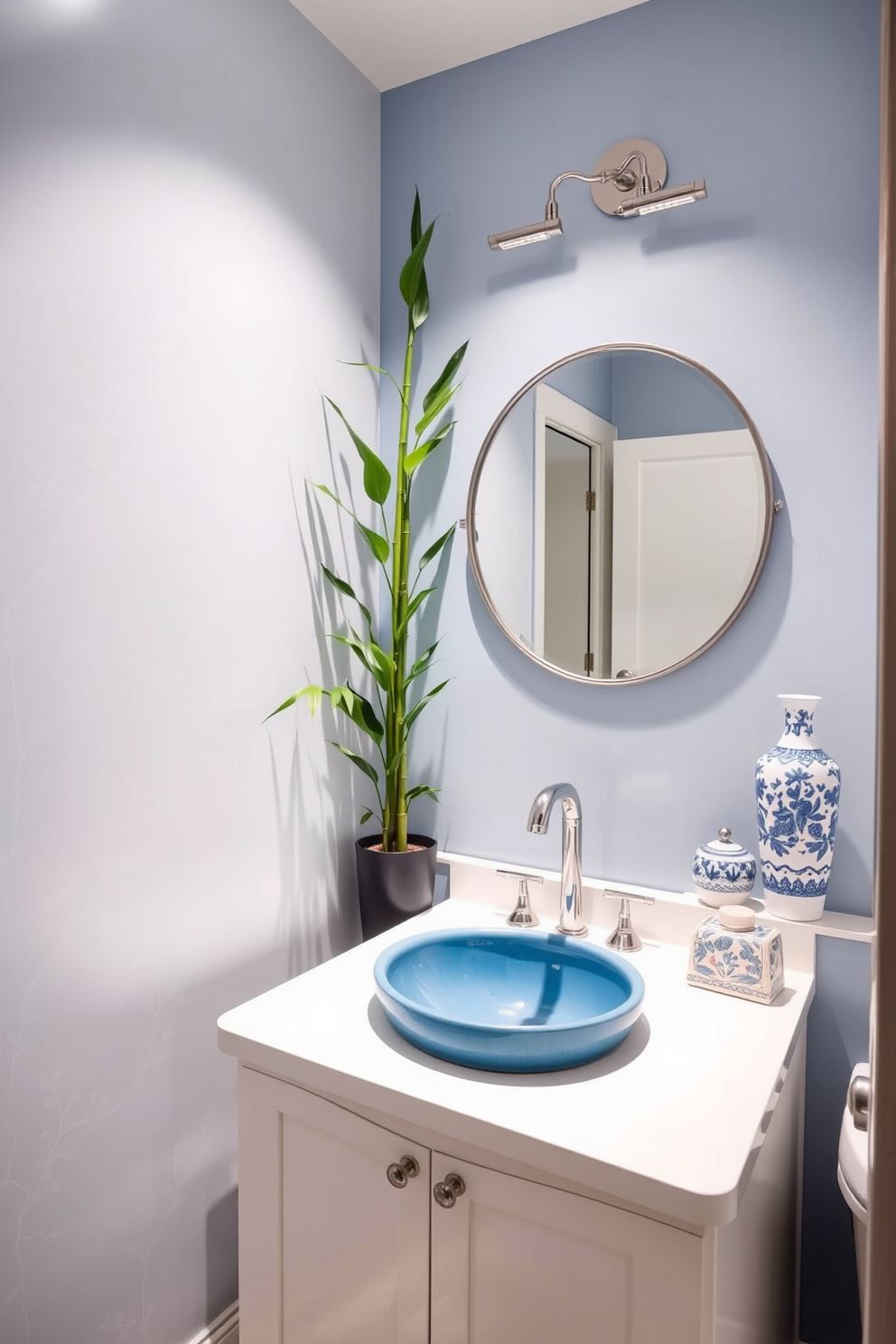 A serene powder room featuring calming blue and white tones. The walls are adorned with delicate Asian-inspired wallpaper, and a sleek white vanity with a blue ceramic sink sits beneath an elegant round mirror. A tall bamboo plant adds a touch of nature to the corner, while decorative blue and white ceramics are placed on the countertop. Soft lighting illuminates the space, creating a tranquil ambiance perfect for relaxation.