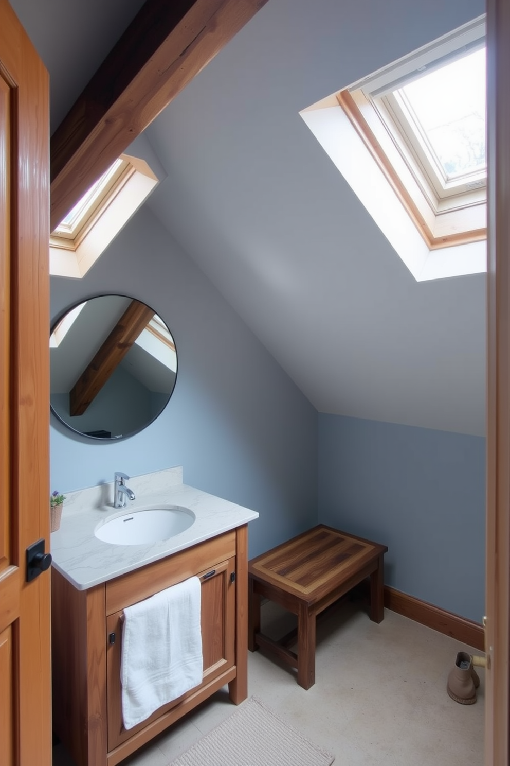 A cozy attic bathroom featuring sloped ceilings and skylights that let in natural light. The space includes a wooden vanity with a marble countertop and a large round mirror above it. To the side, a small bench provides convenience and additional seating. The walls are painted in a soft blue hue, complementing the rustic wooden beams overhead.