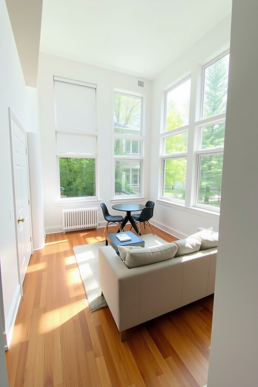 A cozy basement apartment with large windows that allow natural light to flood the space. The walls are painted in a soft white, creating an airy feel, while the flooring is a warm hardwood that adds comfort. The living area features a plush sectional sofa in a neutral tone, paired with a modern coffee table. A small dining nook is set up near the windows, with a round table and stylish chairs that invite casual meals and conversations.