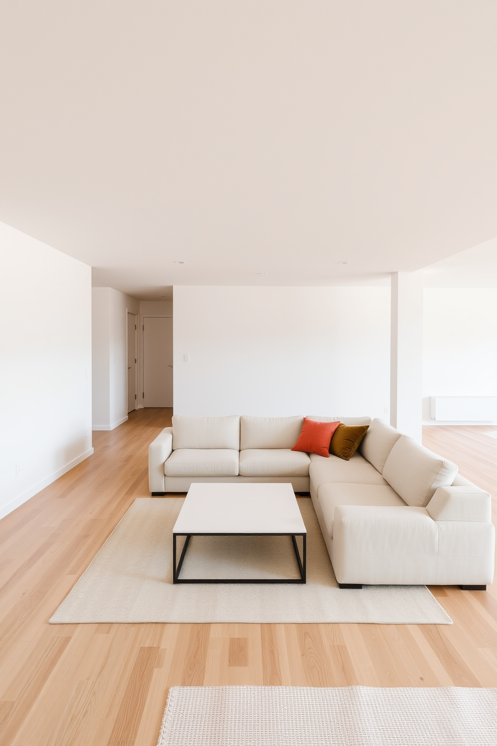 A minimalist basement design featuring a spacious open layout. The walls are painted in soft white tones, and the flooring consists of light hardwood for a warm, inviting feel. The area is furnished with a sleek, low-profile sectional sofa in a light beige fabric. A simple coffee table with clean lines sits at the center, complemented by a few decorative cushions in muted earth tones.