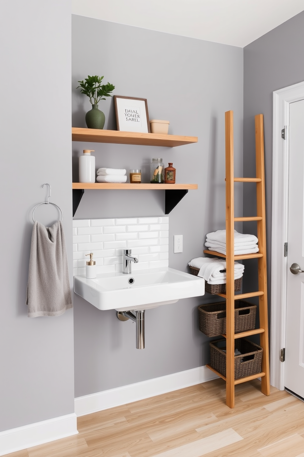 Open shelving above a sleek, modern sink provides easy access to essential toiletries and decorative items. The walls are painted in a soft gray, complemented by a stylish backsplash featuring white subway tiles. A minimalist wooden ladder serves as a unique storage solution, holding neatly folded towels and baskets for additional organization. The flooring is a durable, light-colored laminate that adds warmth to the space while ensuring easy maintenance.