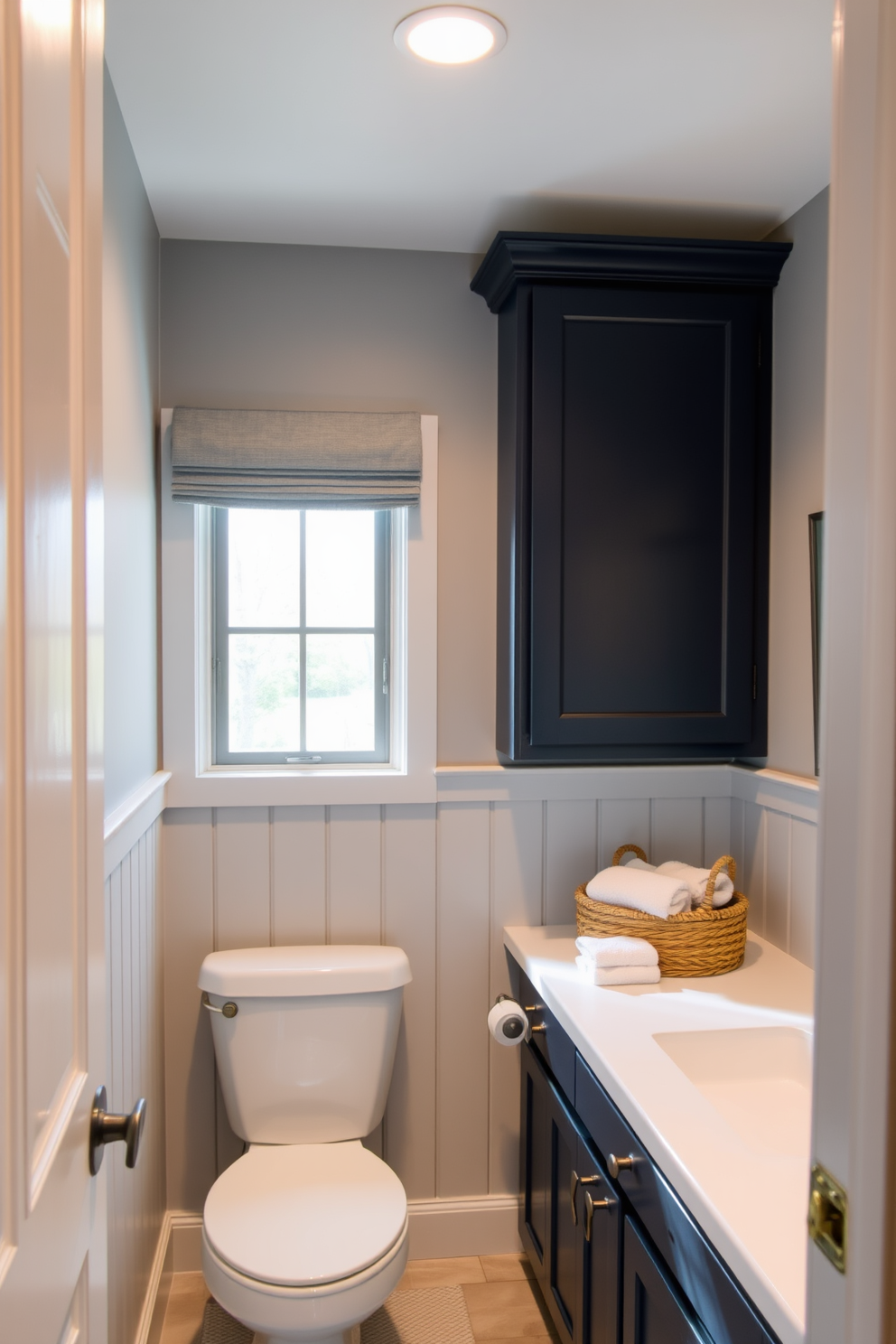 A cohesive color palette featuring soft blues and warm grays creates a serene atmosphere in the basement washroom. The walls are painted in a light gray tone, complemented by navy cabinetry and white fixtures for a balanced look. Natural light filters in through a frosted window, illuminating the space and enhancing the tranquil color scheme. Textured elements like a woven basket and plush towels add warmth and comfort to the design.