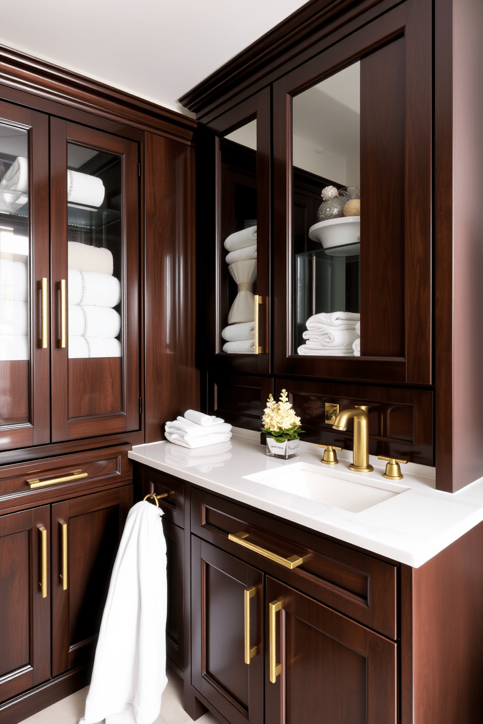 Elegant cabinetry with gold hardware accents. The cabinets feature a rich dark wood finish complemented by sleek gold handles, creating a luxurious feel. The upper cabinets have glass doors showcasing neatly arranged towels and decorative items. Below, a spacious vanity with a white countertop provides ample storage while enhancing the overall elegance of the bathroom.