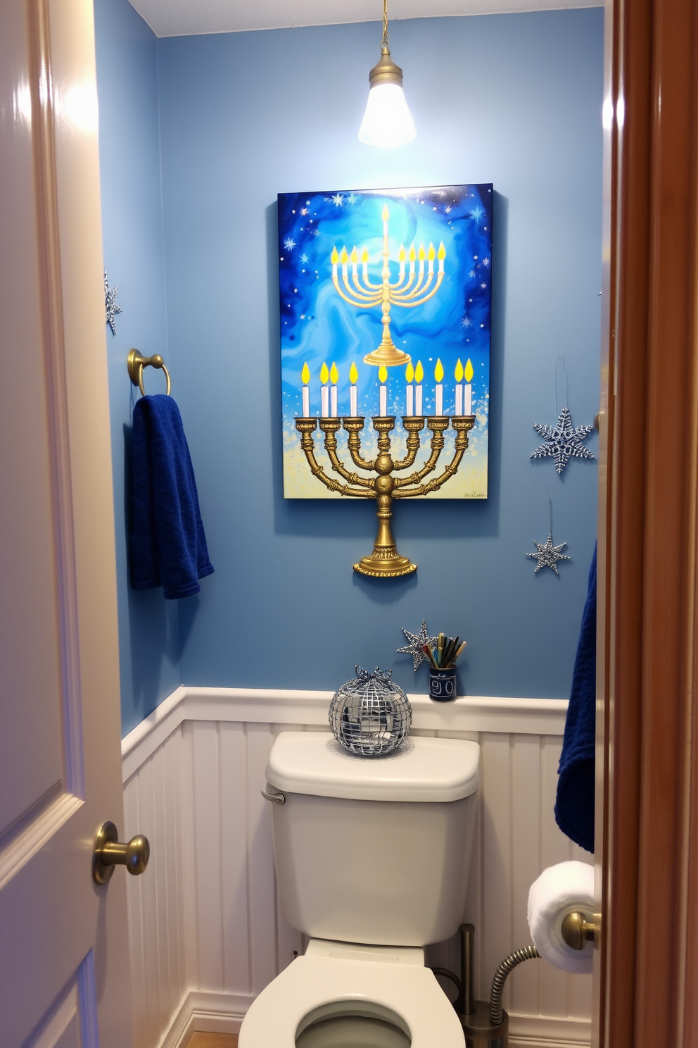 A cozy bathroom decorated for Hanukkah features a beautiful piece of artwork depicting a menorah hung above the toilet. The walls are adorned with blue and silver accents, and festive decorations like dreidels and stars enhance the holiday spirit.