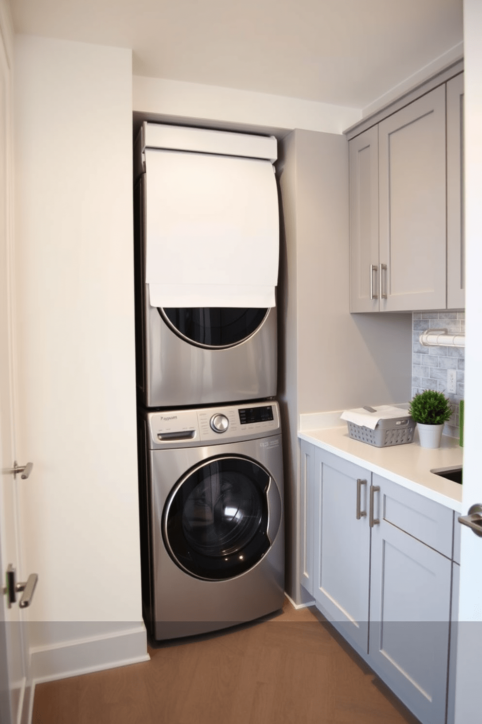 A modern laundry room featuring a sleek laundry chute integrated into the wall for easy access. The space includes a stacked washer and dryer, surrounded by custom cabinetry in a soft gray finish, with a countertop for folding clothes. Bright white walls enhance the open feel, while a stylish backsplash adds a pop of color behind the appliances. A laundry basket sits neatly beside the machines, and a small potted plant brings a touch of nature to the design.