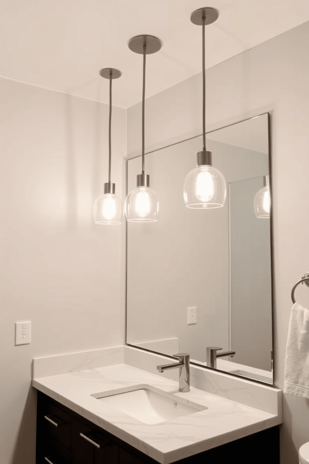 A sleek bathroom lighting design featuring modern pendant lights suspended above the vanity area. The lights have a minimalist design with a brushed nickel finish, casting a warm glow over the marble countertop below.