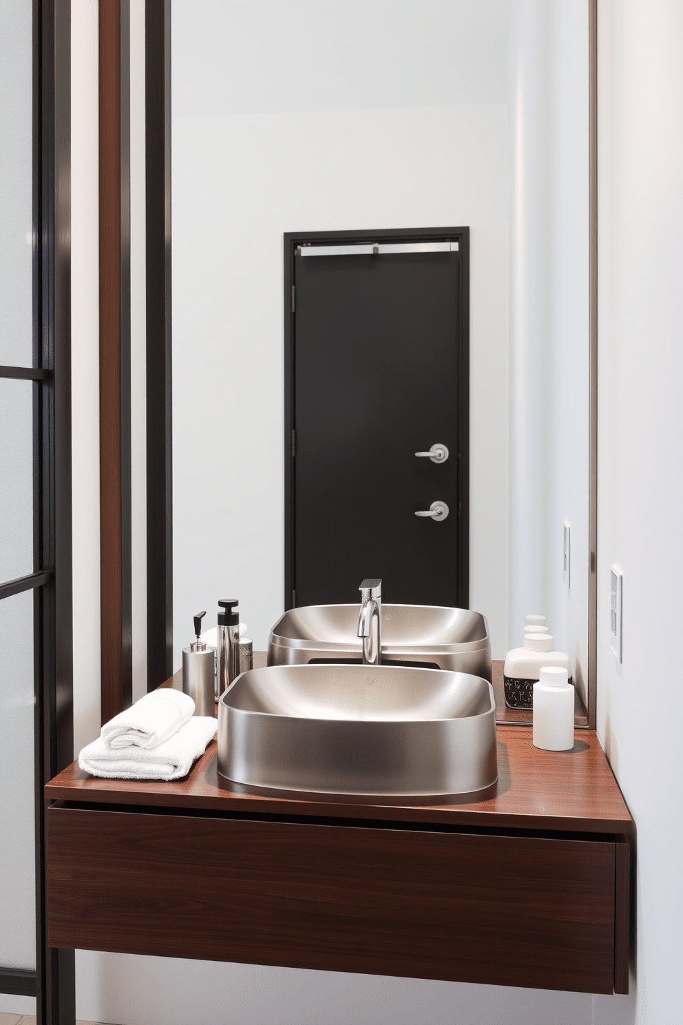 A sleek stainless steel sink is the focal point of a modern bathroom design. It is paired with a minimalist faucet that complements the clean lines and contemporary aesthetic of the space. The sink is installed in a floating vanity made of dark wood, providing a striking contrast against the light-colored walls. Surrounding the sink, elegant accessories and a neatly folded towel add a touch of sophistication to the overall look.