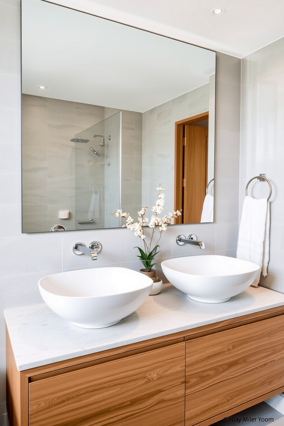 A modern bathroom featuring double vessel sinks positioned on a sleek wooden vanity with a polished stone countertop. Above the sinks, stylish wall-mounted faucets complement the contemporary design, while a large mirror reflects the elegant space. The walls are adorned with soft gray tiles, creating a serene backdrop for the sinks. Decorative elements such as potted plants and luxurious towels enhance the inviting atmosphere of this shared bathroom space.