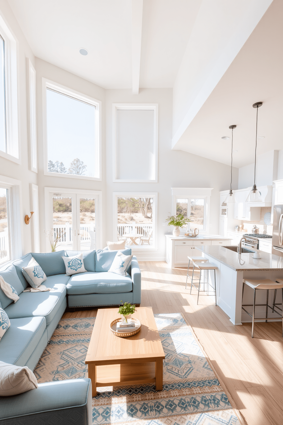 A bright and airy open floor plan with large windows allowing natural light to flood the space. The living area features a comfortable sectional sofa in soft blue tones, paired with a light wooden coffee table and coastal-inspired decor. Adjacent to the living area, a modern kitchen boasts sleek white cabinetry and stainless steel appliances. A spacious island with bar stools provides a casual dining option, accented by pendant lighting overhead.