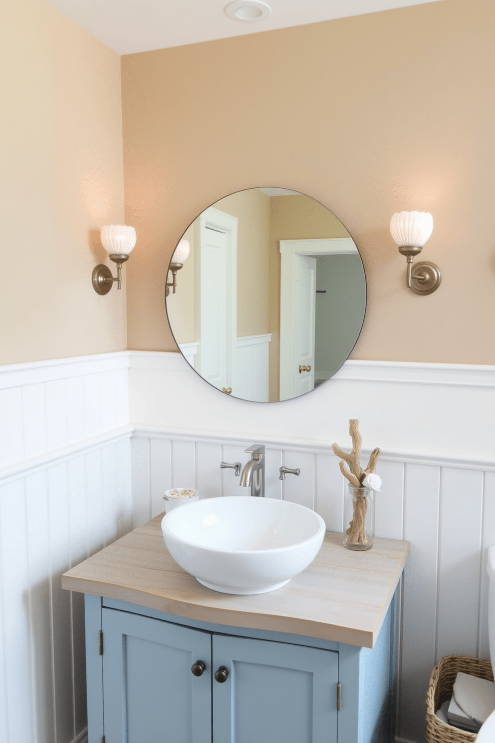 A beach bathroom design featuring sconces with nautical elements. The walls are painted in a soft sandy beige, complemented by white wainscoting and driftwood accents. The sconces, shaped like seashells, provide warm ambient lighting on either side of a large round mirror. A wooden vanity with a light blue finish holds a white vessel sink, while marine-themed decor adds a playful touch.