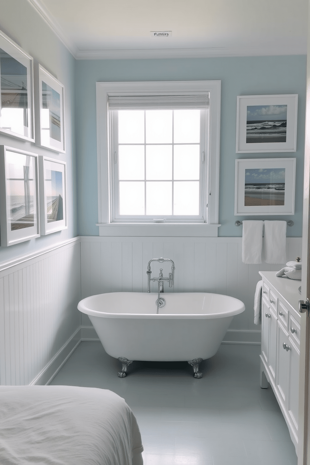 Framed beach photography adorns the walls, capturing serene coastal scenes that evoke a sense of tranquility. The photographs are arranged in a gallery style, complemented by soft white frames that enhance the beachy aesthetic. The bathroom features a light blue color palette, reminiscent of the ocean waves. A freestanding soaking tub sits beneath a large window, allowing natural light to flood the space and highlight the beach-themed decor.