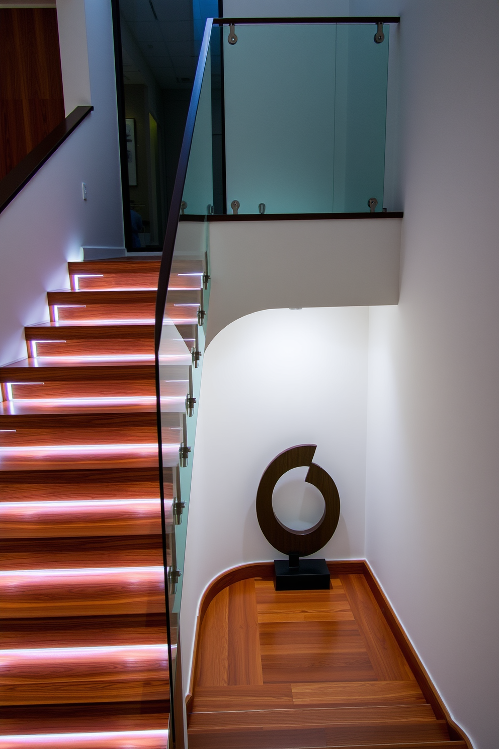 A stunning staircase with integrated lighting features seamlessly blends functionality and elegance. The steps are crafted from rich hardwood, and soft LED lights illuminate the edges, creating a warm and inviting atmosphere. The balustrade is made of sleek glass, providing an unobstructed view of the space below. At the base, a modern art piece complements the staircase design, enhancing the overall aesthetic.