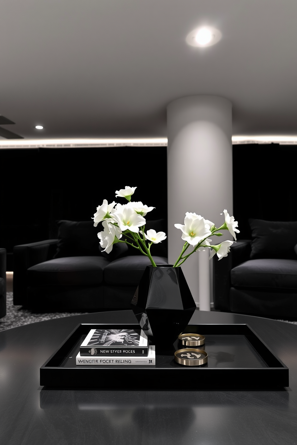 A stylish black coffee table centerpiece features a sleek geometric vase filled with fresh white flowers. Surrounding the vase are a few carefully arranged coffee table books and a set of elegant coasters. The black basement design showcases a cozy lounge area with plush seating in deep gray tones. Ambient lighting highlights the textured walls, creating an inviting atmosphere perfect for relaxation and entertainment.