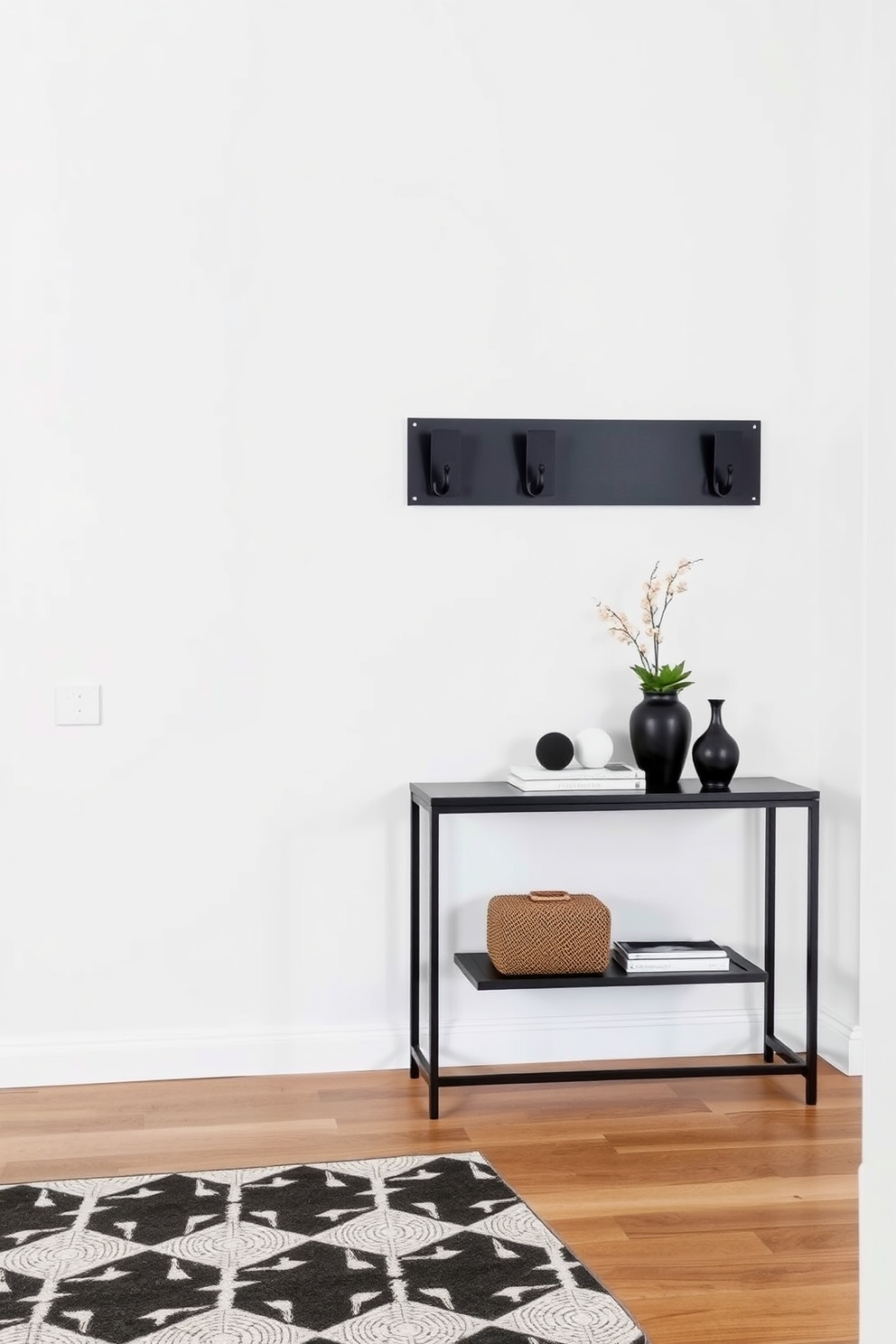 A sleek foyer featuring contemporary black wall hooks mounted on a crisp white wall. The floor is adorned with a geometric patterned rug that adds warmth to the space, while a stylish console table sits against the wall, topped with decorative items and a small potted plant.