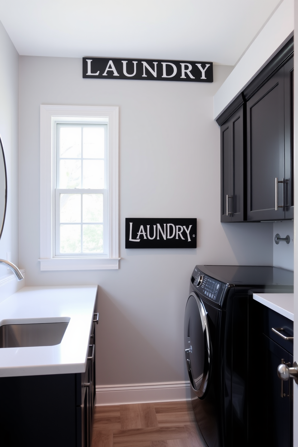 A stylish black laundry sign is prominently displayed on the wall, adding a touch of personality to the space. The laundry room features sleek black cabinetry paired with white countertops for a modern contrast. The walls are painted in a soft gray hue, creating a calming backdrop for the room. A large window allows natural light to flood in, illuminating the space and enhancing the overall aesthetic.