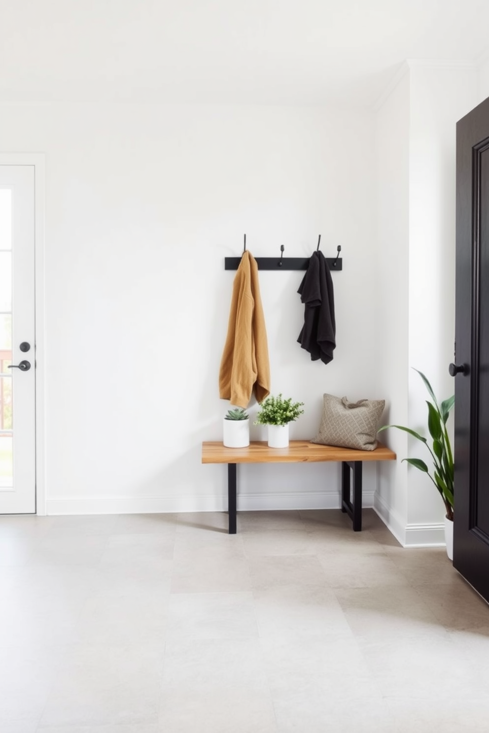 A minimalist mudroom features sleek black hooks mounted on a light-colored wall, providing a functional yet stylish storage solution. The floor is covered with large, neutral-toned tiles that complement the simplicity of the space, creating an inviting entryway. Incorporating a bench made of natural wood adds warmth to the design, while a few potted plants introduce a touch of greenery. The overall aesthetic is clean and uncluttered, perfect for a modern home.