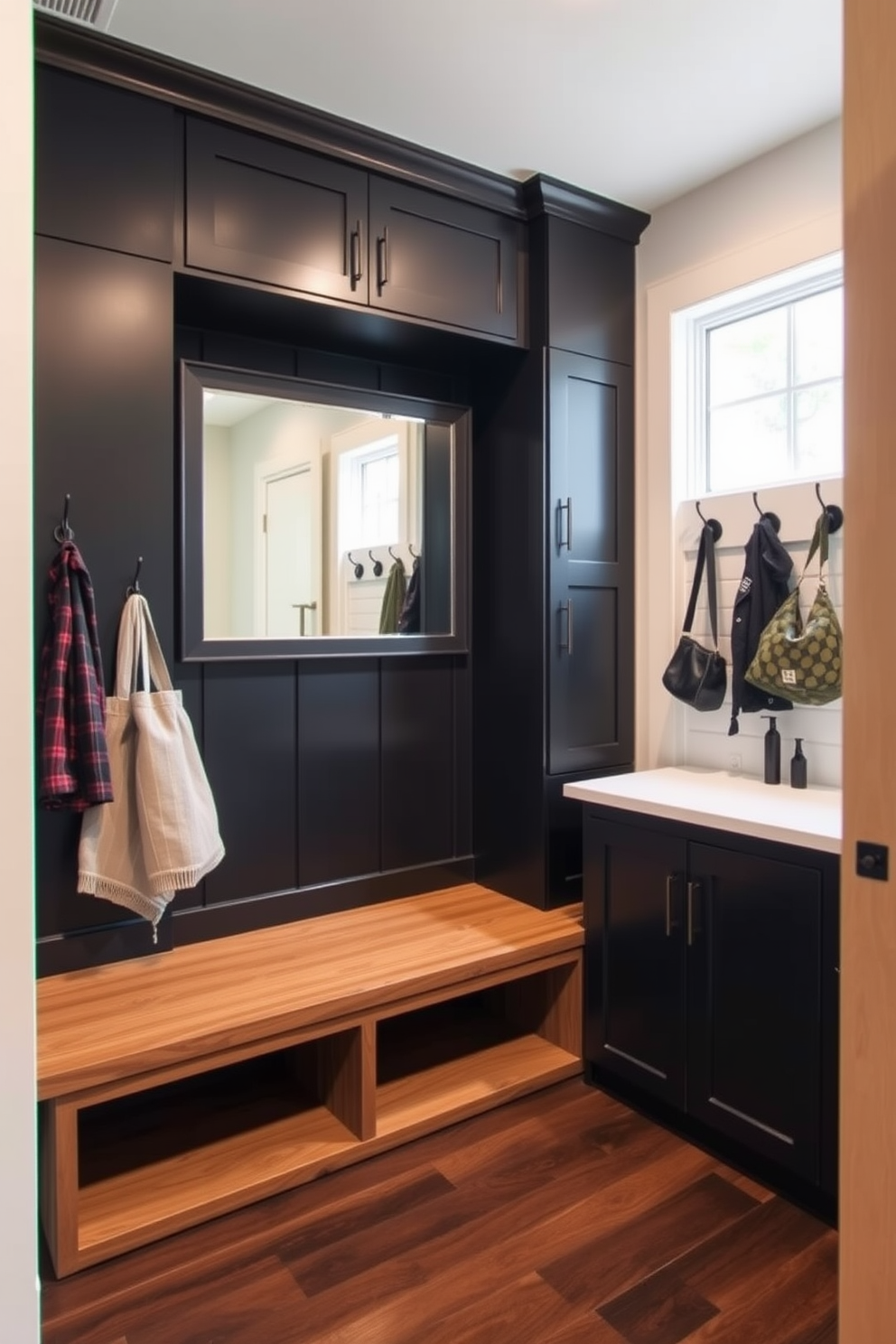 A stylish mudroom featuring a sleek black and wood combination. The space includes a built-in wooden bench with storage underneath, accented by black hooks on the wall for hanging coats and bags. The flooring is a dark wood that complements the black cabinetry, creating a cohesive look. A large mirror is mounted above the bench, enhancing the sense of space and functionality in this practical entryway.