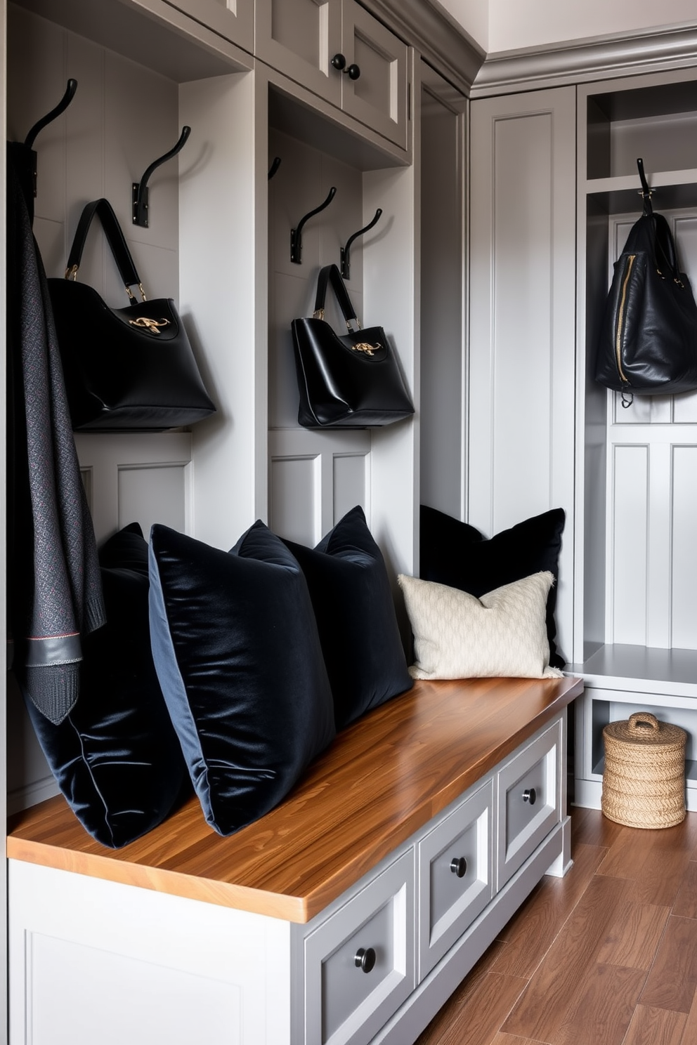 Luxurious black velvet cushions adorn a sleek wooden bench in an elegant mudroom. The space features ample storage with custom cabinetry painted in a soft gray, complemented by stylish hooks for coats and bags.