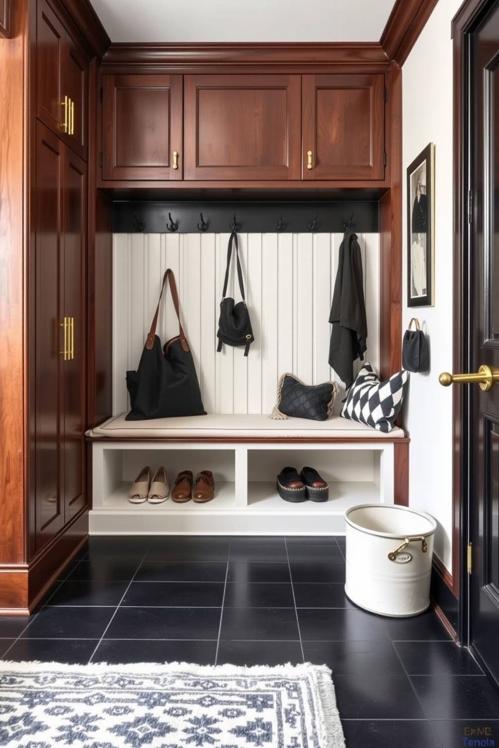 A stylish mudroom featuring classic black accents and brass hardware. The space includes a built-in bench with storage underneath, complemented by hooks for coats and bags, all framed by rich wood paneling. The floor is adorned with large black tiles that contrast beautifully with a light-colored wall. Brass fixtures and hardware add a touch of elegance, while a patterned area rug brings warmth and texture to the room.