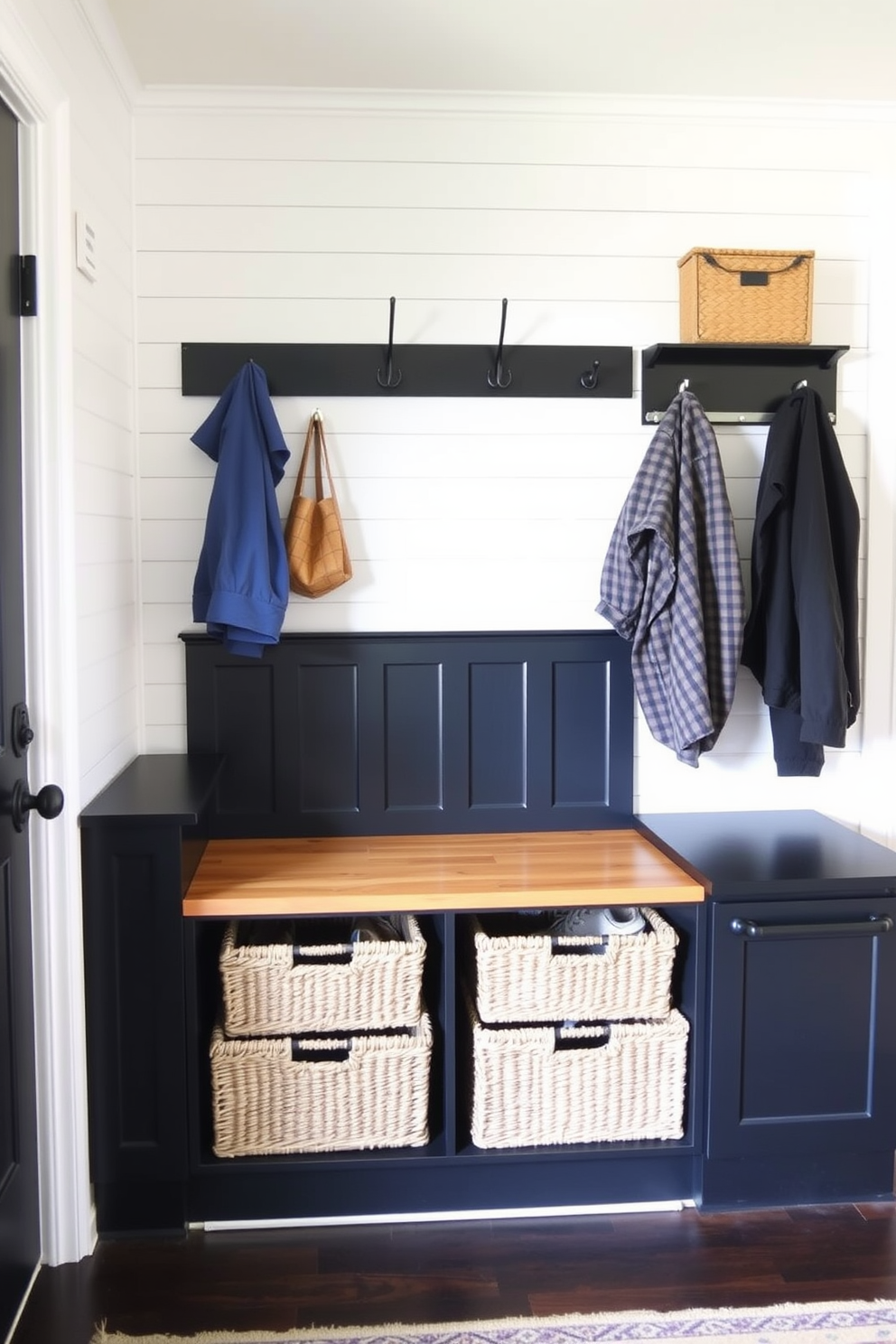 A stylish mudroom featuring a combination of black and natural wood elements. The space includes a built-in bench with a natural wood seat and black cabinetry, providing ample storage for shoes and outdoor gear. The walls are adorned with shiplap in a soft white finish, contrasting with the dark wood accents. A large black coat rack hangs above the bench, while woven baskets in natural tones are neatly organized below for added functionality.