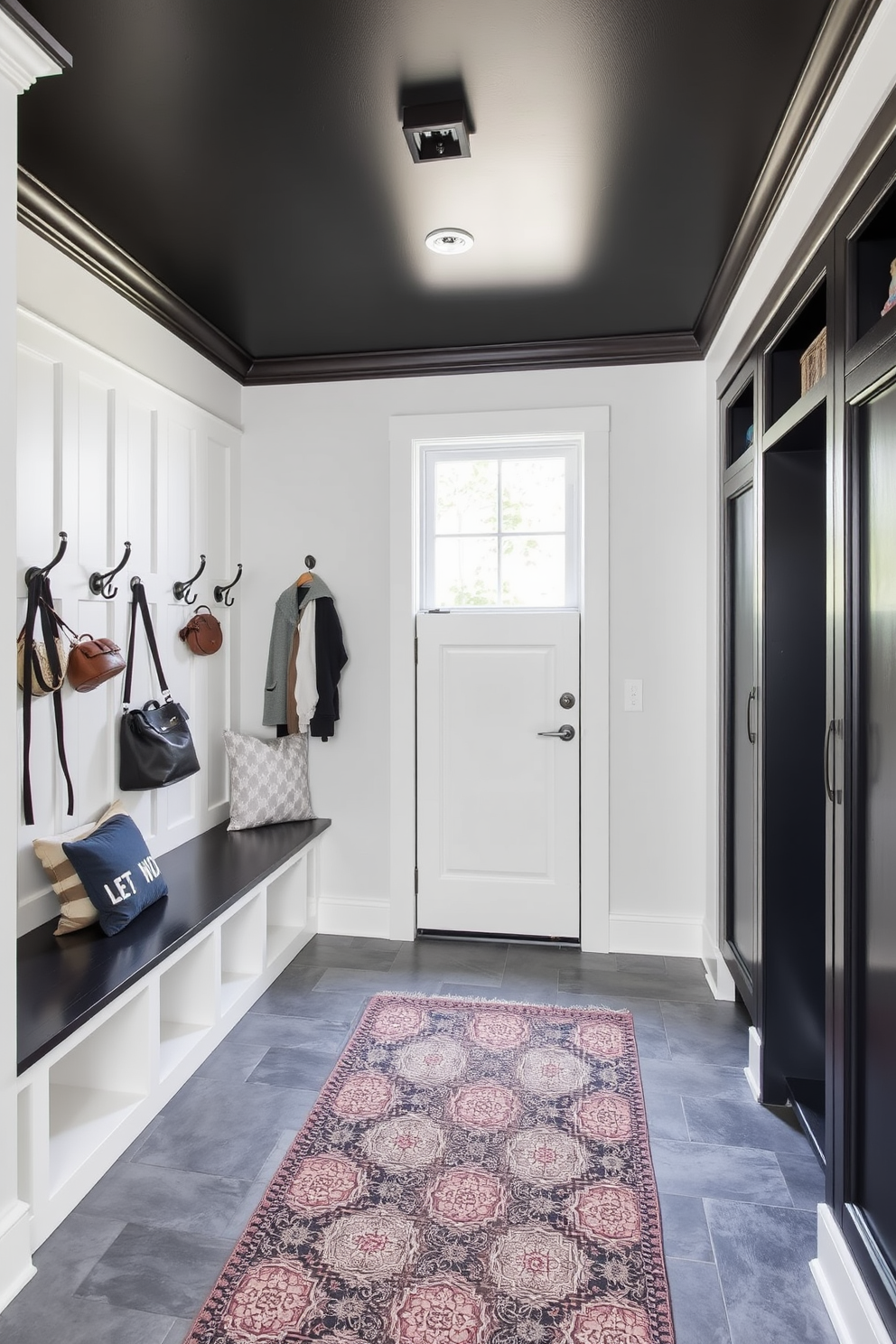 A striking mudroom with a black painted ceiling that adds a dramatic effect to the space. The walls are a crisp white, contrasting beautifully with the dark ceiling, while a built-in bench with storage cubbies provides functionality and style. The floor is adorned with large gray tiles, providing durability and an elegant touch. Hooks line the walls for hanging coats and bags, and a stylish area rug adds warmth and color to the entryway.