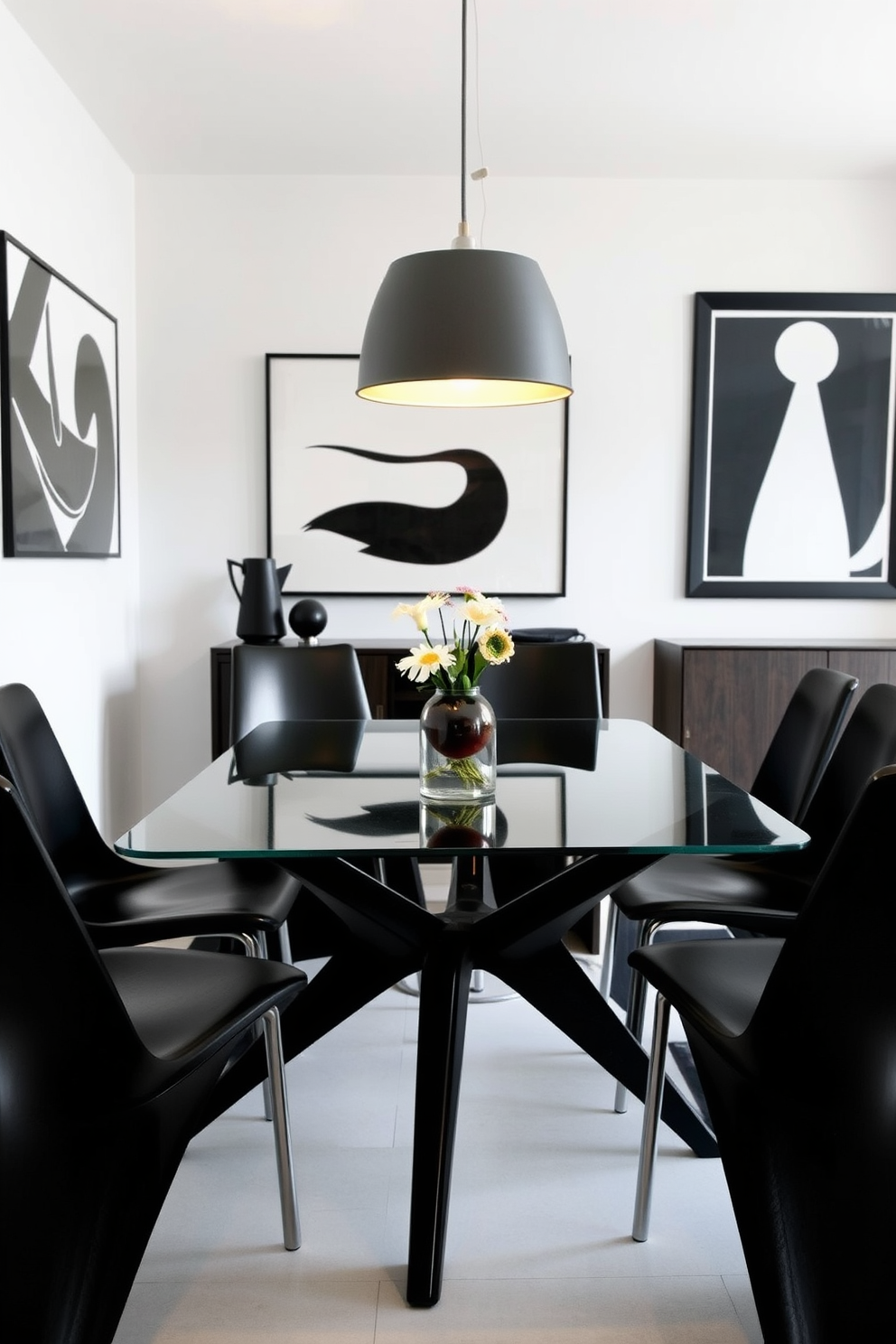 A contemporary dining room features a sleek glass table supported by elegant black legs. Surrounding the table are modern black chairs with minimalist designs, creating a striking contrast against the bright white walls. The room is adorned with bold black and white artwork, adding a touch of sophistication to the space. A stylish pendant light hangs above the table, casting a warm glow that enhances the inviting atmosphere.