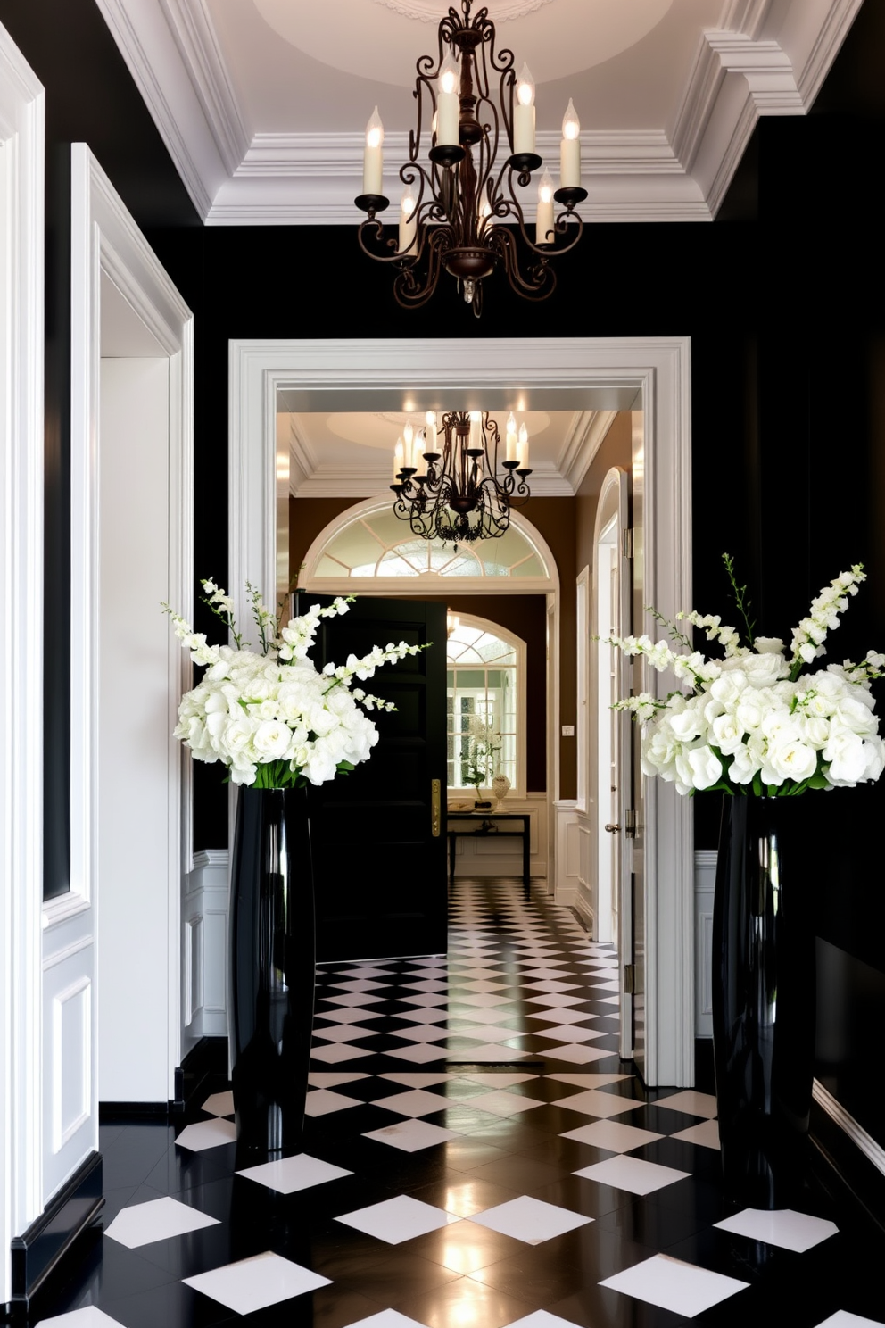 Elegant white molding frames the entrance of the foyer, creating a striking contrast against the bold black accents. The floor is adorned with a black and white checkerboard pattern, enhancing the sophisticated atmosphere of the space. A grand chandelier hangs from the ceiling, illuminating the area with a warm glow. Flanking the entrance are tall black vases filled with lush white flowers, adding a touch of elegance and life to the design.