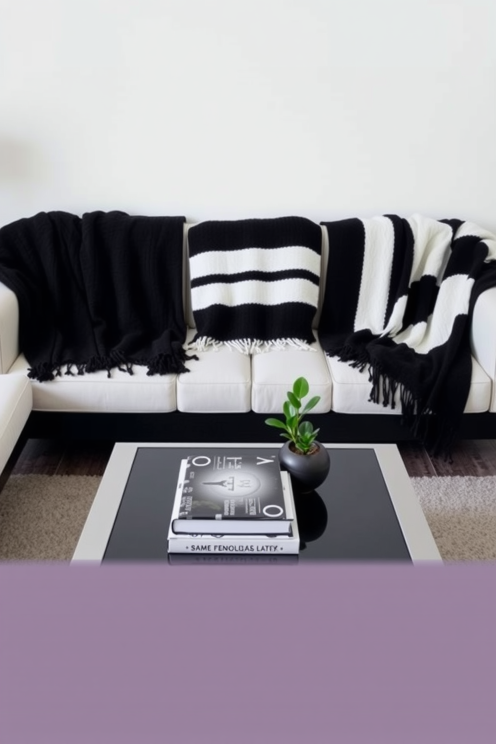 A stylish living room featuring contrasting black and white throw blankets draped over a modern sofa. The walls are painted in a crisp white, while a sleek black coffee table sits at the center, adorned with decorative books and a small plant.