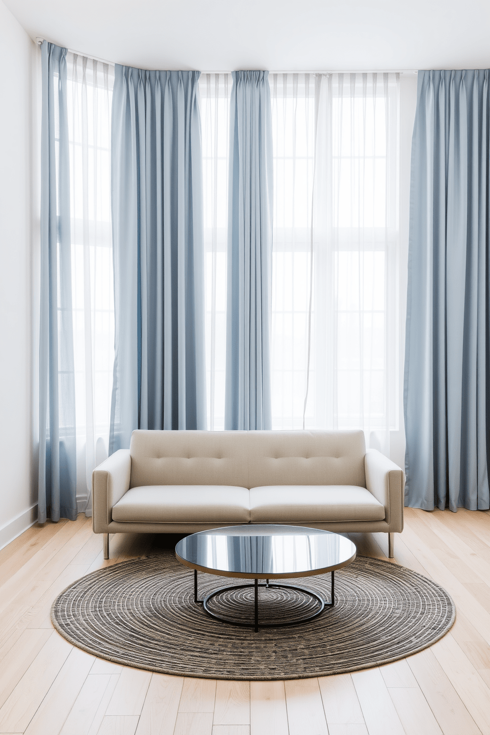 A serene minimalist living space featuring dusty blue curtains that gently frame large windows. The walls are painted in a soft white, and the floor is adorned with light wooden planks, creating a calm and airy atmosphere. In the center of the room, a sleek, low-profile sofa in a neutral tone complements the curtains. A round coffee table with a glass top sits atop a textured area rug, adding warmth and sophistication to the space.