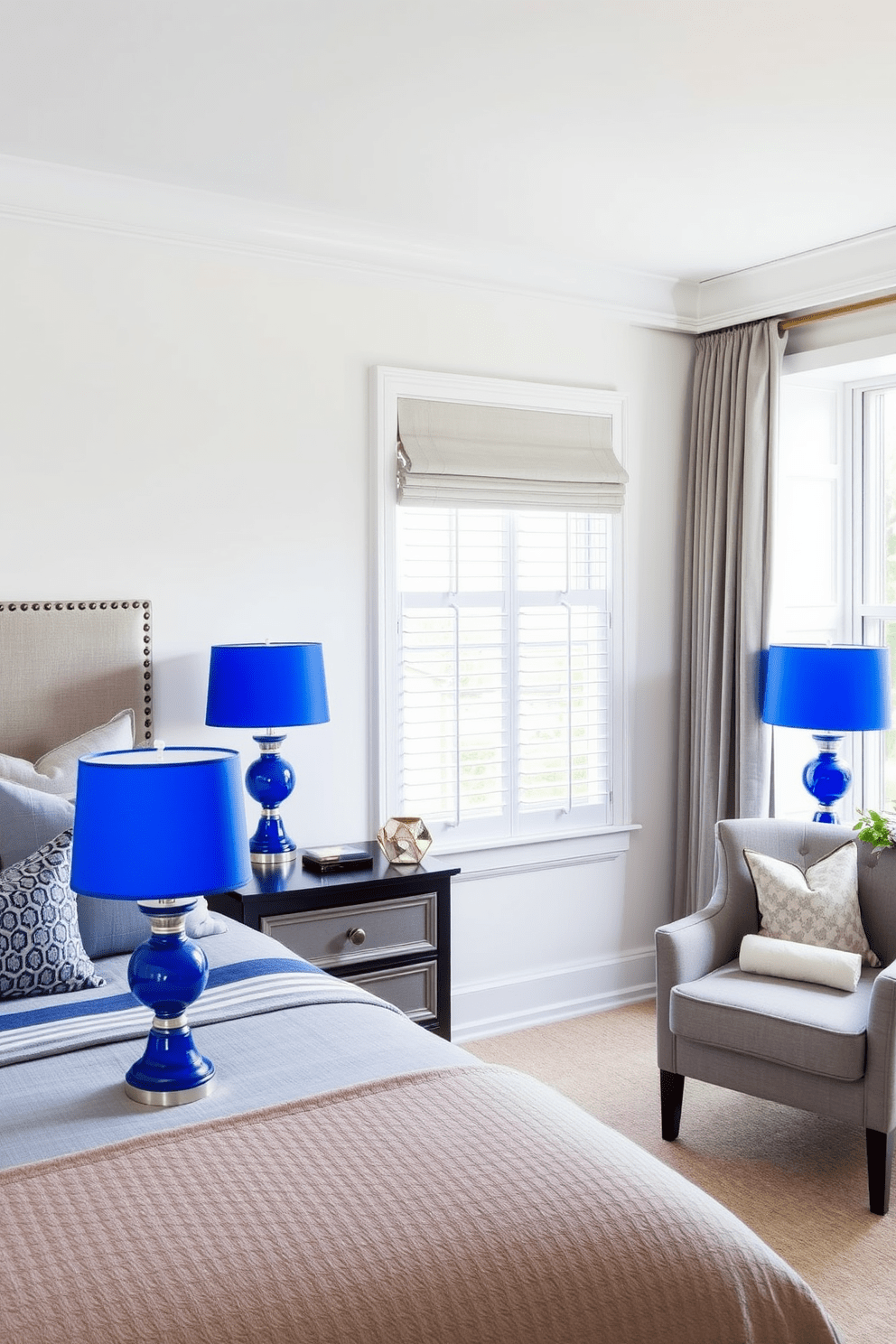 A chic bedroom featuring cobalt blue lamps on elegant nightstands that complement the overall decor. The walls are painted in a soft white, creating a bright and inviting atmosphere. The bed has a plush upholstered headboard with coordinating bedding in shades of blue and gray. A cozy reading nook is situated by the window, adorned with a stylish armchair and a small side table.