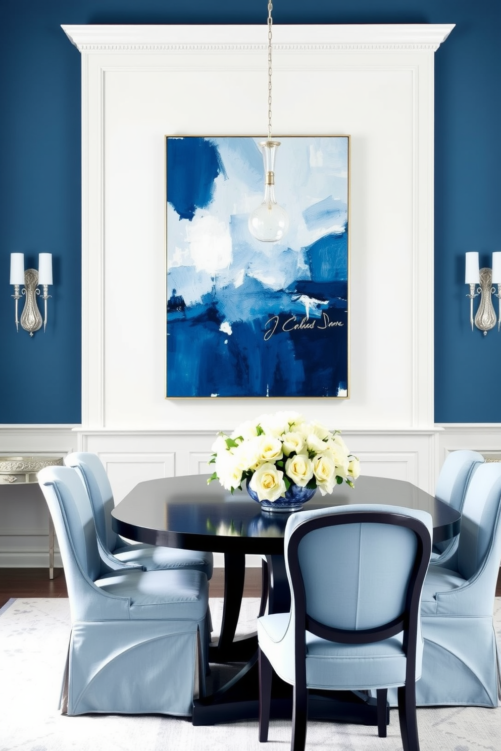 A serene dining room featuring shades of blue throughout the space. The walls are painted in a soft powder blue while the furniture includes a dark navy dining table surrounded by light blue upholstered chairs. The centerpiece is a stunning arrangement of white flowers in a blue vase on the table. A large abstract painting in varying shades of blue hangs on the wall, complemented by elegant silver accents in the decor.