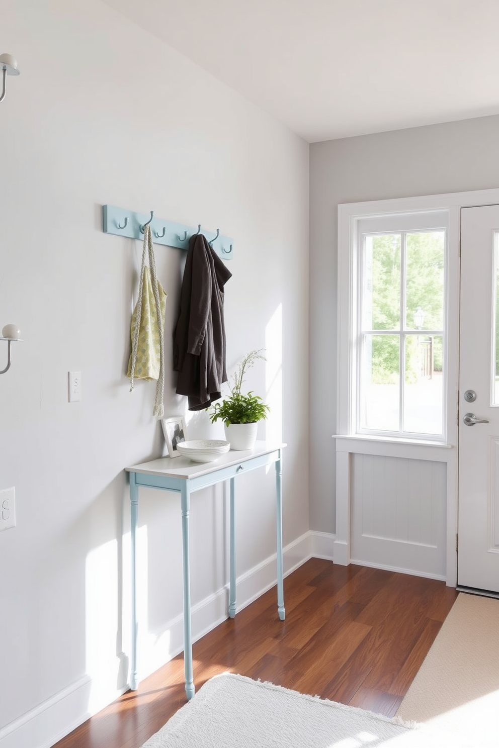 A pastel blue coat rack with multiple hooks is positioned against a light gray wall, providing a cheerful and functional entryway feature. The floor is adorned with a soft white rug that complements the pastel tones, creating a welcoming atmosphere. In the foyer, natural light streams in through a large window, illuminating a small console table beneath the coat rack. Decorative items such as a potted plant and a stylish bowl sit atop the table, enhancing the overall design while maintaining a clean and organized look.