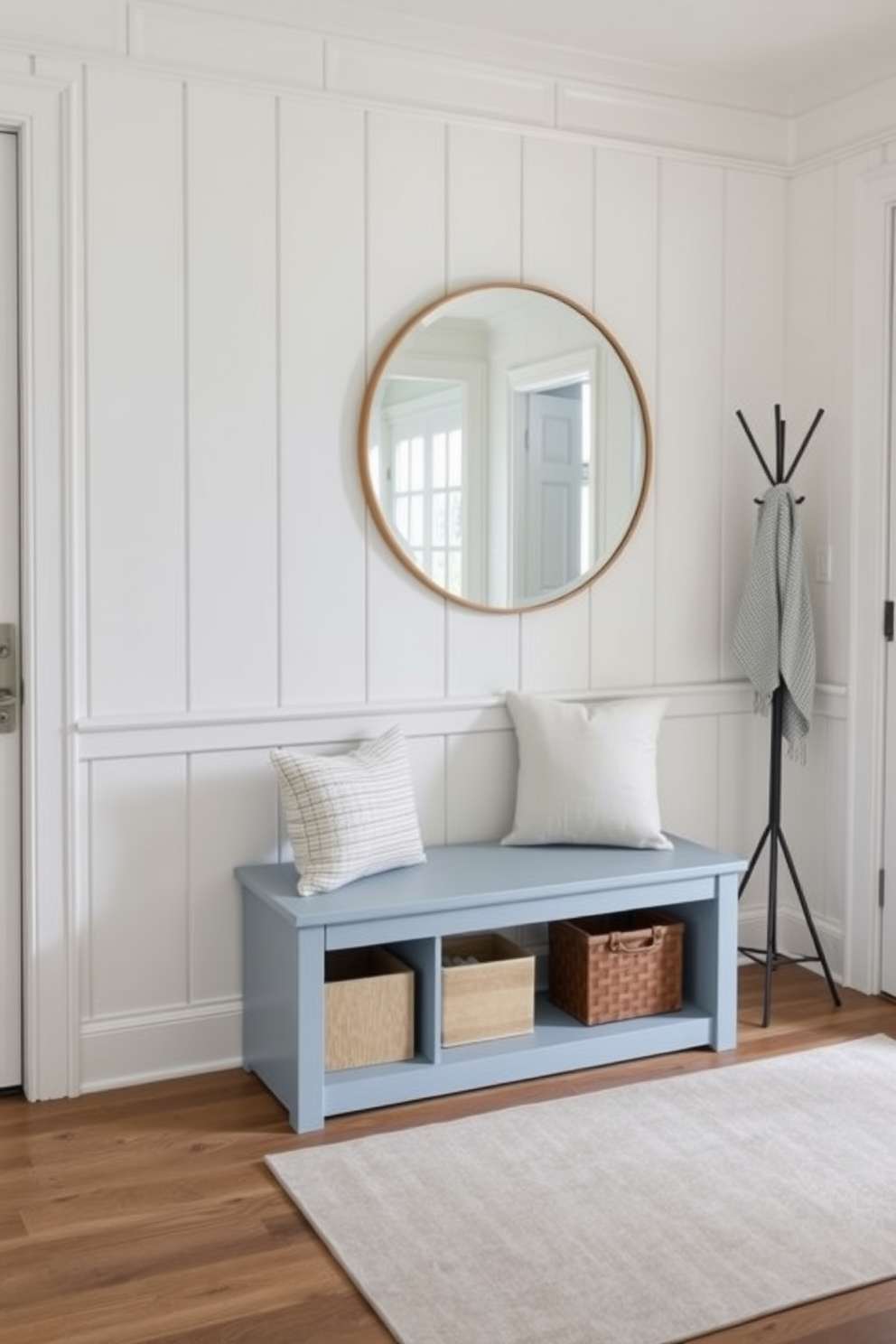 A light blue bench with storage underneath is positioned in a welcoming foyer. The walls are adorned with soft white paneling, complementing the bench's color and creating an airy atmosphere. To the side, a stylish coat rack adds functionality, while a large round mirror above the bench enhances the sense of space. A subtle area rug in neutral tones anchors the design, inviting guests into the home.