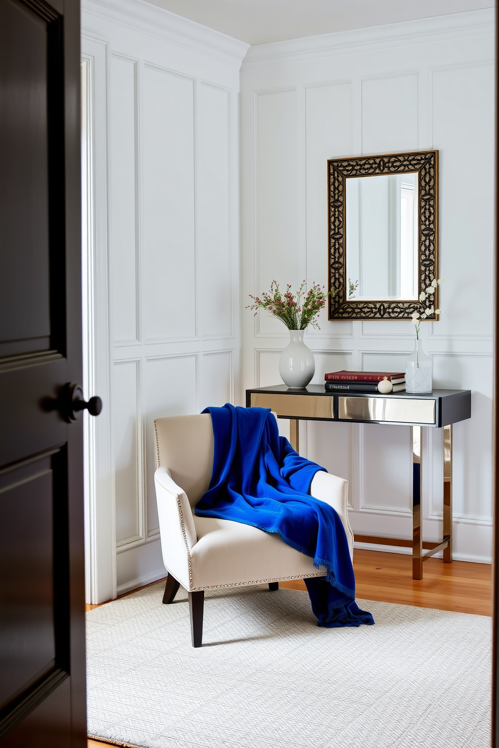 A cozy foyer featuring a sapphire blue throw blanket draped elegantly over a stylish chair. The walls are adorned with soft white paneling, and a sleek console table stands against the wall, complemented by a decorative mirror above it.