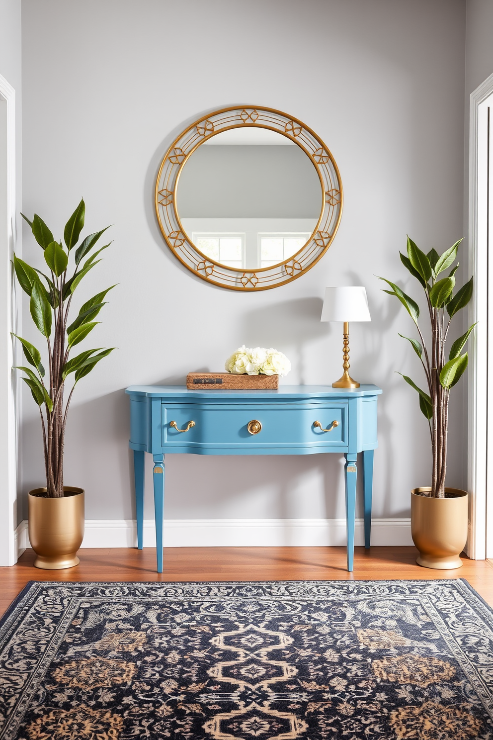 An ocean blue console table with elegant gold hardware stands against a light gray wall. The foyer features a stylish area rug with intricate patterns that complement the table's color, creating a welcoming atmosphere. Flanking the console table are two tall potted plants that add a touch of greenery. Above the table, a large round mirror with a decorative frame enhances the sense of space and light in the foyer.