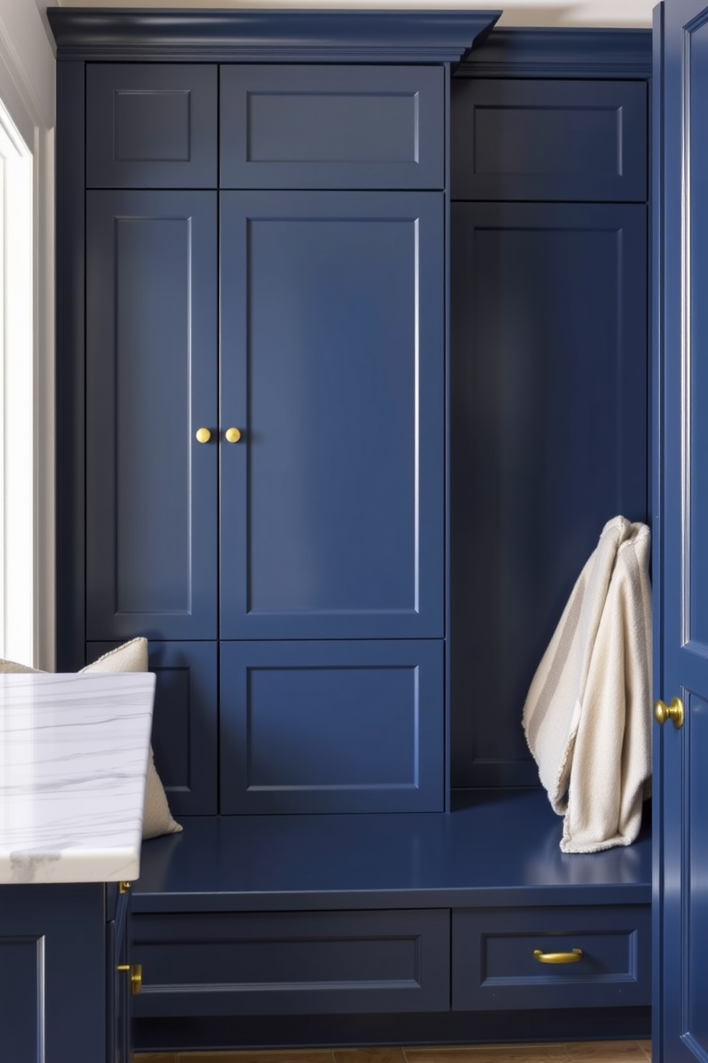 A stylish mudroom featuring dark blue cabinetry with a polished marble countertop. The cabinetry is complemented by brass hardware and a built-in bench with plush cushions for comfort.