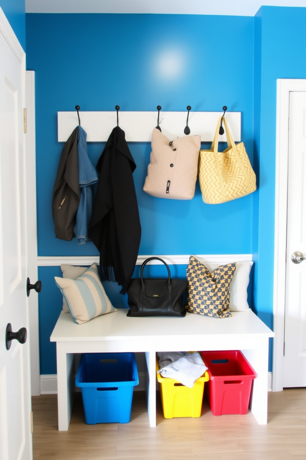 A bright blue accent wall features stylish hooks for hanging coats and bags. The mudroom is designed with a functional bench for seating, complemented by colorful storage bins beneath.