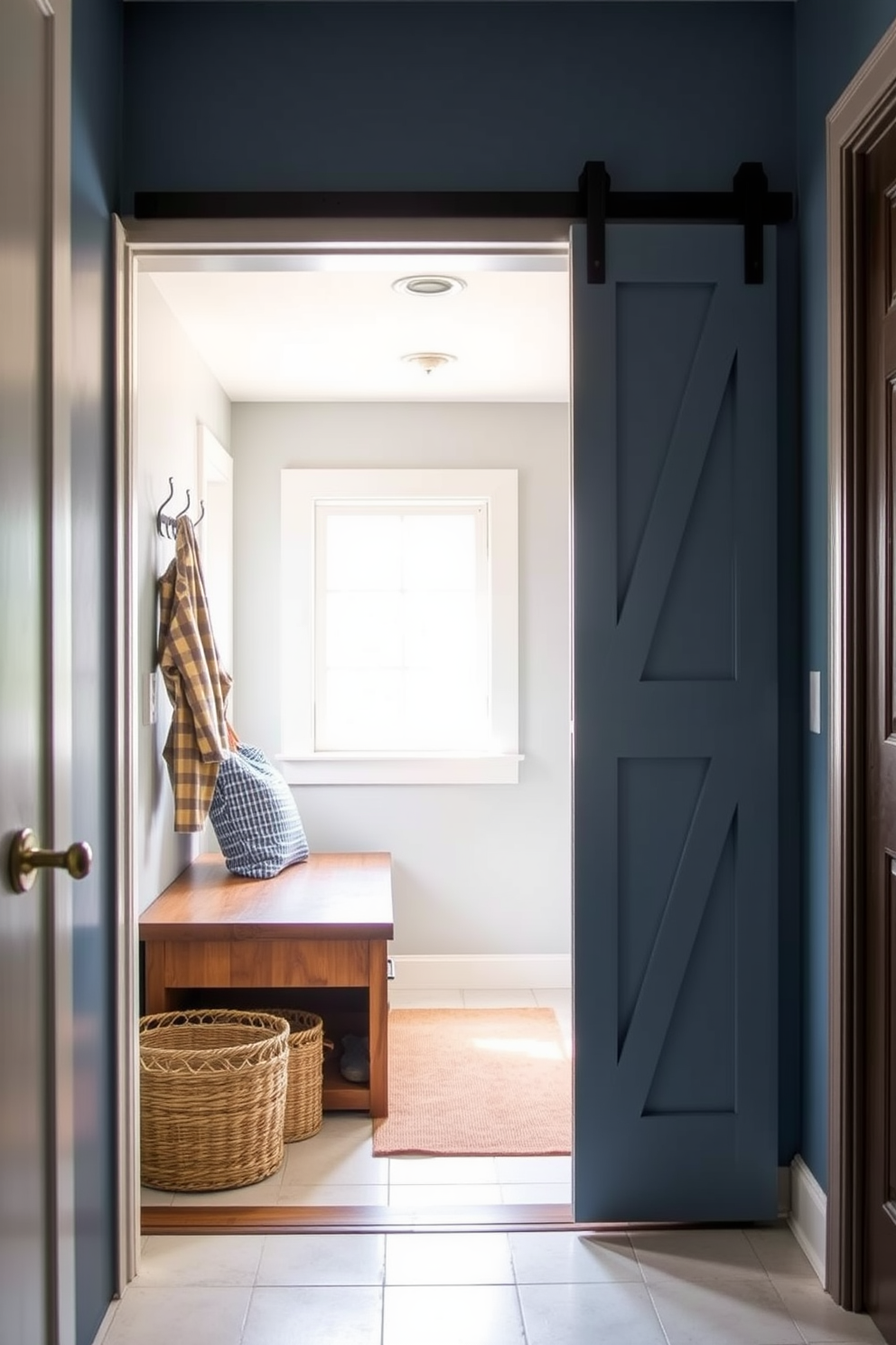 A blue mudroom featuring sliding barn doors opens up to a spacious area with a rustic charm. The walls are painted a soft blue, complemented by a wooden bench with storage underneath and hooks for coats and bags. Natural light floods the space through a large window, illuminating the light-colored tile floor. A woven basket sits beside the bench, adding a cozy touch while keeping the area organized.