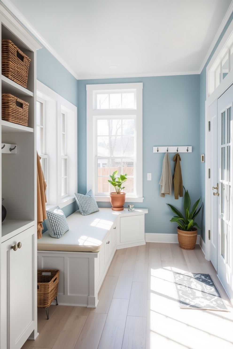 A serene mudroom bathed in natural light features soft blue walls that create a calming atmosphere. The space includes built-in benches with plush cushions and open shelving adorned with decorative baskets for storage. Large windows allow sunlight to flood the room, highlighting the light wood flooring that complements the blue tones. A stylish coat rack and a set of hooks provide practical organization, while potted plants add a touch of greenery.