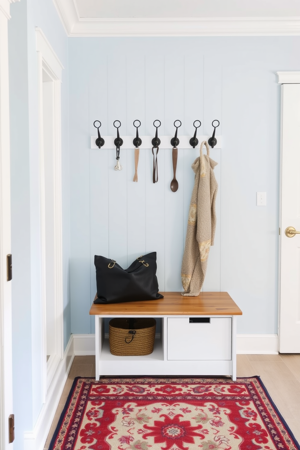 Light blue mudroom featuring vintage hooks mounted on the wall. The space includes a wooden bench with storage underneath and a patterned rug on the floor.