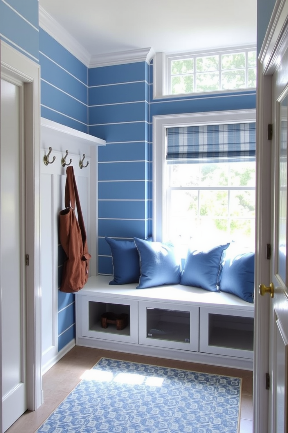 A charming mudroom featuring blue and white striped wallpaper that creates a fresh and inviting atmosphere. The space includes a built-in bench with storage underneath, adorned with plush cushions in coordinating blue tones. To the left, there are hooks for coats and bags, crafted from brushed nickel for a modern touch. Natural light floods the room through a large window, illuminating a patterned area rug that adds warmth to the tiled floor.