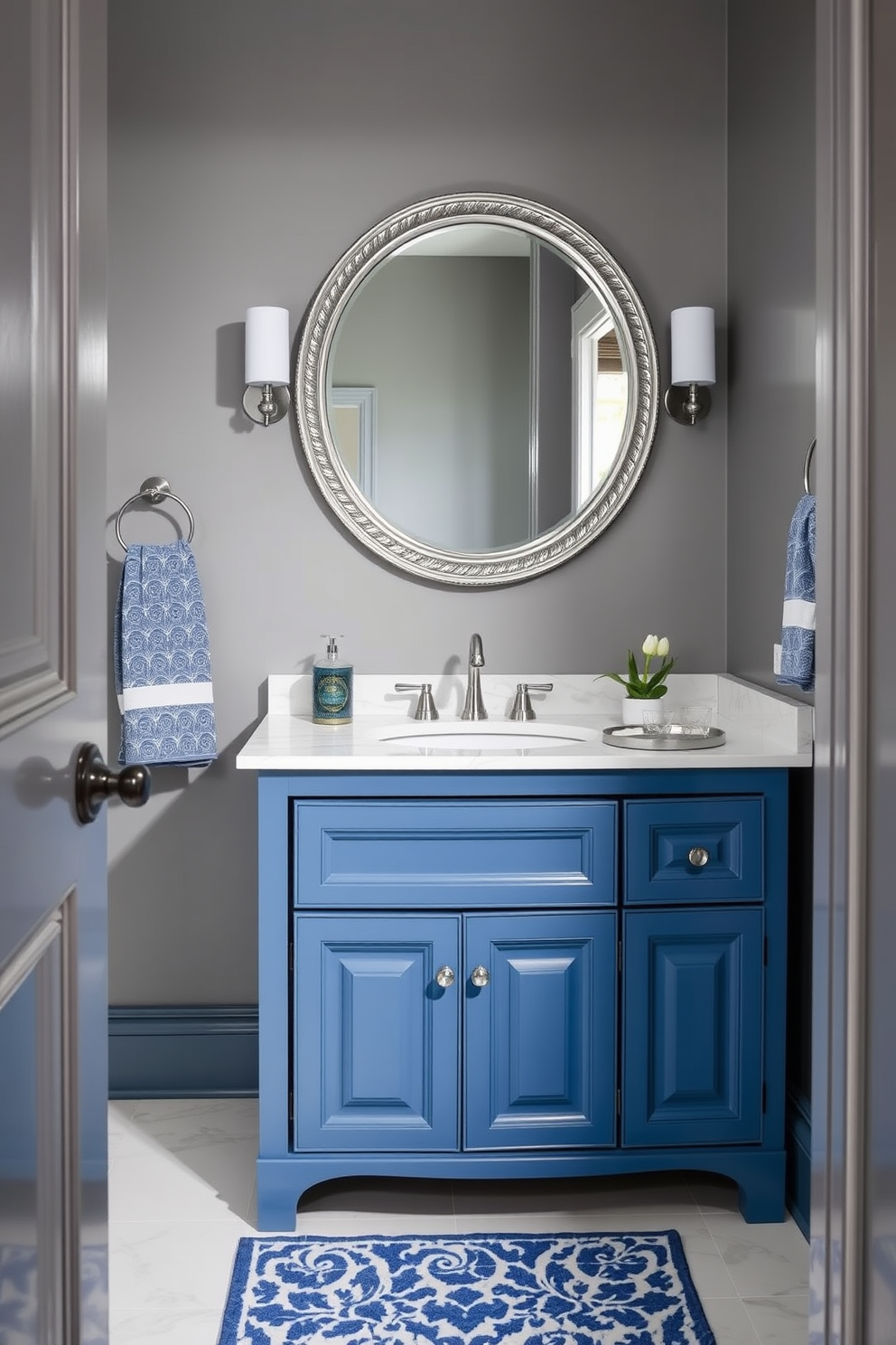 A classic blue and gray powder room features a stunning blue vanity with a white marble countertop. The walls are painted in a soft gray, providing a serene backdrop for the elegant decor. A large round mirror with a silver frame hangs above the vanity, reflecting the stylish fixtures. Decorative accents include a blue and white patterned rug and matching towels that enhance the cohesive color scheme.