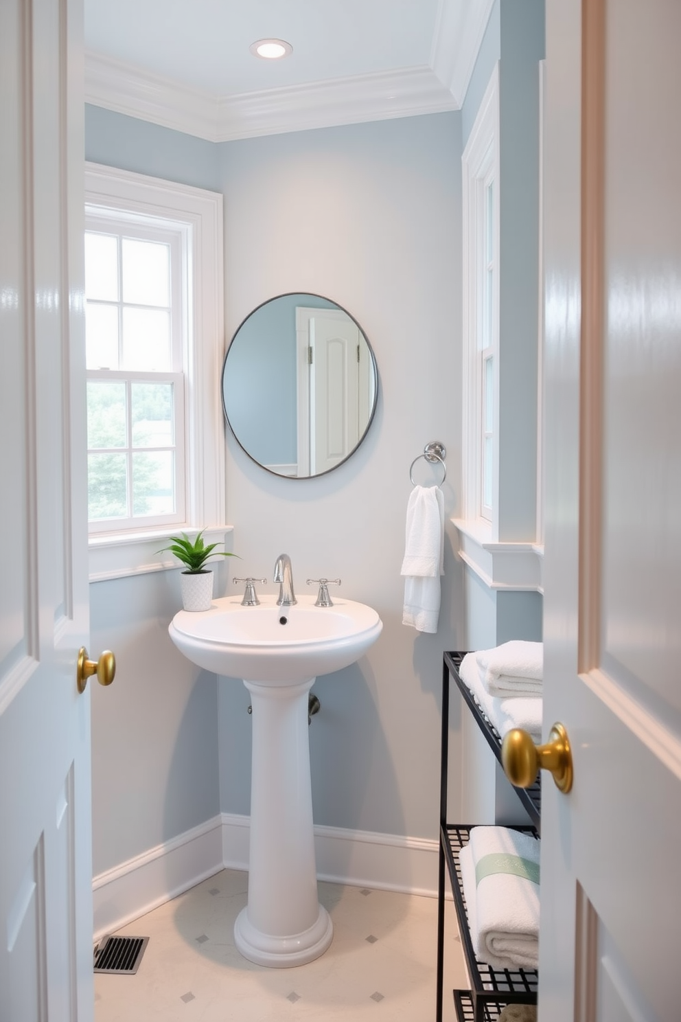 A soft pastel blue powder room features white trim around the windows and door. The walls are painted in a calming pastel blue, creating a serene atmosphere. A sleek white pedestal sink is positioned against one wall, complemented by a stylish round mirror above it. Decorative accents include a small potted plant and elegant hand towels neatly arranged on a nearby shelf.